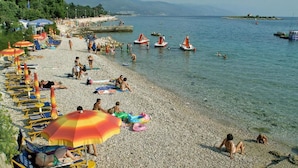 Une plage de galets avec des parasols, des chaises longues et des gens qui se baignent.