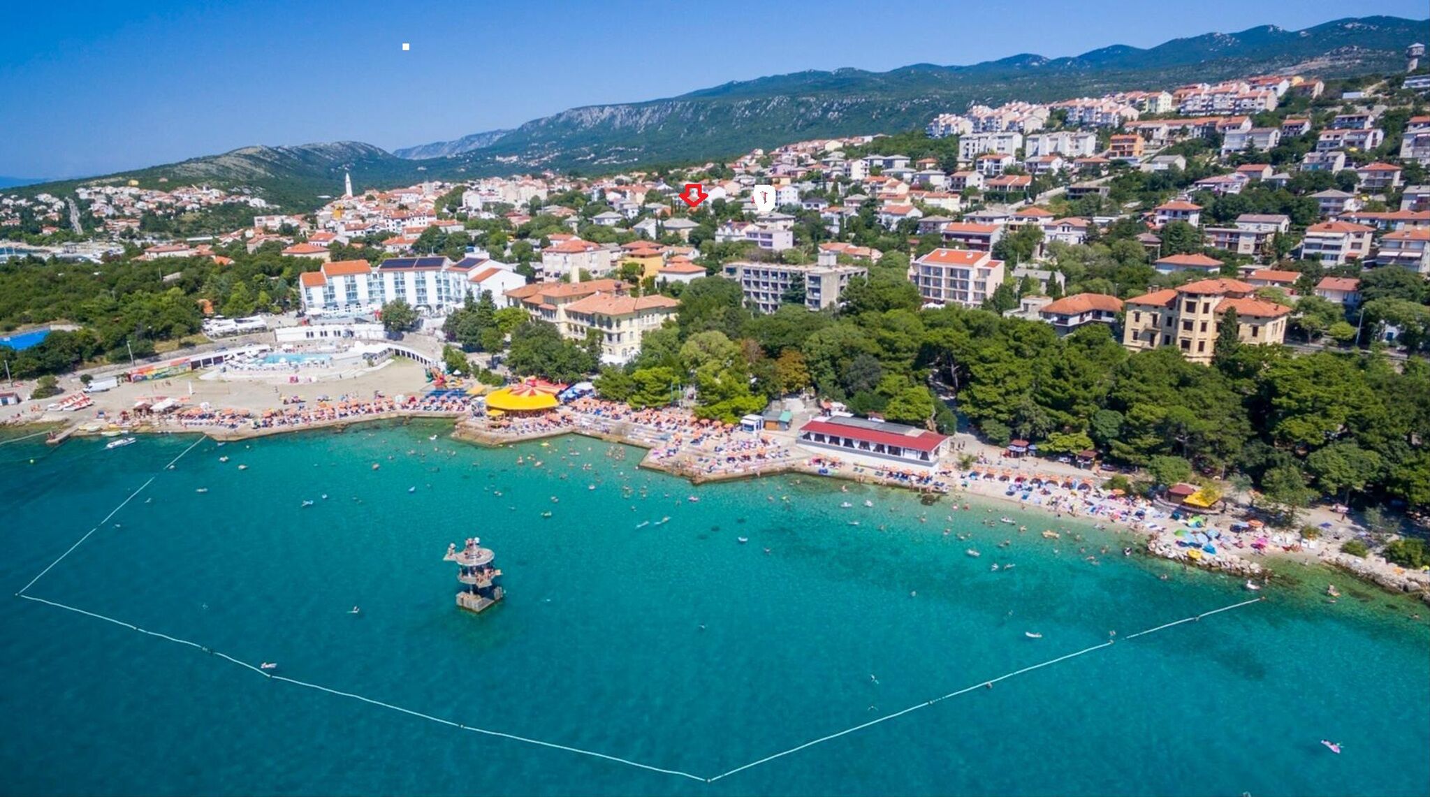 An aerial view of a coastal town with a beach, buildings, and a clear blue sea.