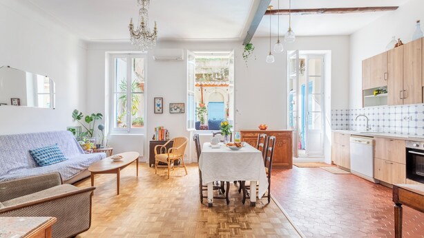 Un salón luminoso con sofá, mesa de comedor y sillas. Cuenta con una zona de cocina con armarios y lavavajillas.