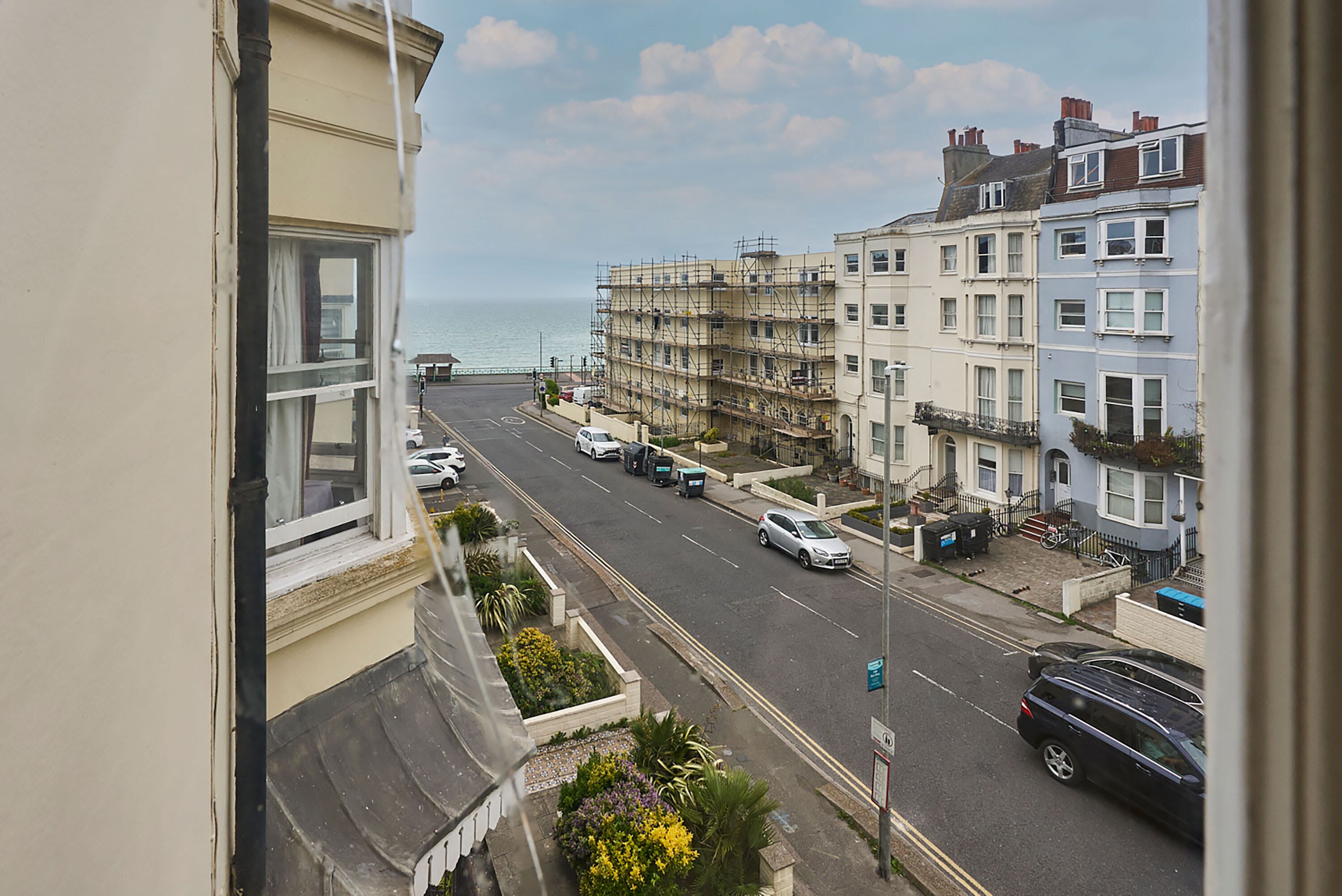 Une vue de rue avec des immeubles, des voitures garées et une vue sur la mer.