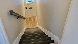 Una scala con corrimano a sinistra, gradini in legno e una porta in cima.