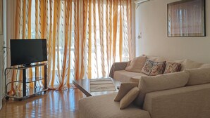 A living room with a sofa, a coffee table, a TV on a stand, and a window with curtains.