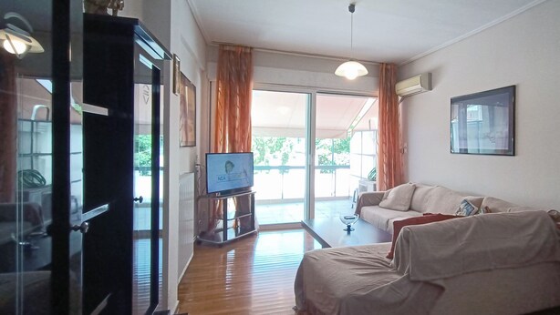 A living room with a sofa, a television, and a glass door leading to a balcony.