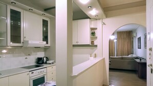 A kitchen with white cabinets, a stove, and a coffee maker. There is a living area with a sofa and a TV.