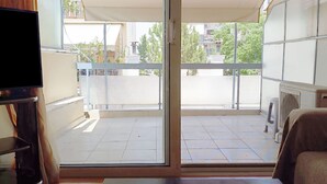 A room with a sliding glass door leading to a balcony. There is a television on the left side and a heater on the right.