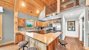 A spacious kitchen with wooden cabinets, a central island with stools, and a stainless steel refrigerator. - Spacious Ellicottville 5-bedroom 4-bath chalet with WiFi, AC (East Otto)