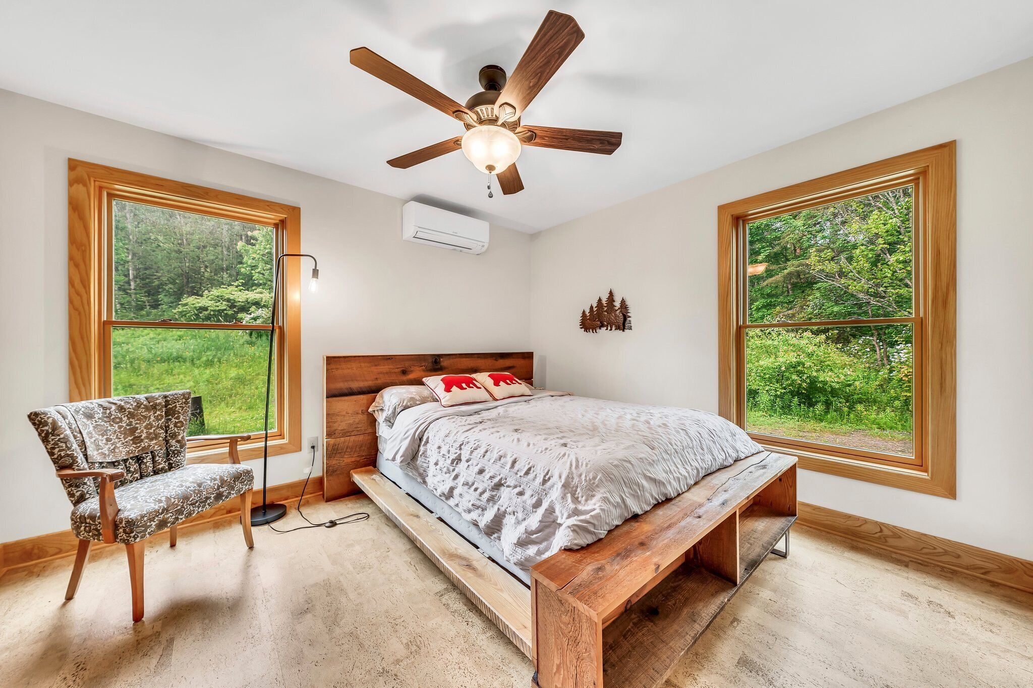 Un dormitorio con cama de madera, un banco de madera, una silla y un ventilador de techo.