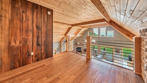 A spacious attic room with wooden floors and a sloped ceiling, featuring a view of a green garden and a stone wall. - Spacious Ellicottville 5-bedroom 4-bath chalet with WiFi, AC (East Otto)