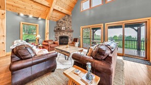 A cozy living room with leather sofas, a fireplace, and large windows offering a view of the outdoors. - Spacious Ellicottville 5-bedroom 4-bath chalet with WiFi, AC (East Otto)