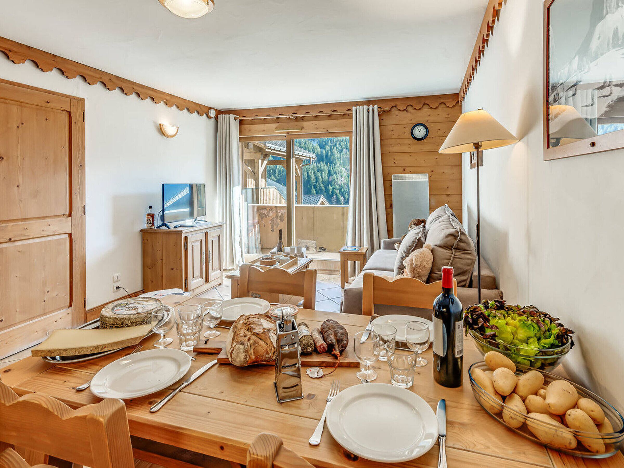 Un coin repas avec une table en bois mise pour le dîner, une bouteille de vin et un saladier rempli de salade.
