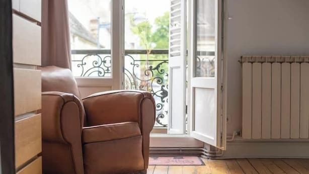 A room with a brown leather chair, a radiator, and a view of a balcony with a metal railing. - Arras • 2 ch • Balcon • Parking gratuit • Standing (Arras)