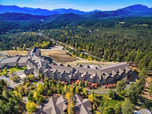 Un hotel gran, de moltes plantes i amb una estructura de teulada complexa, envoltat per una densa vegetació forestal i muntanyes al fons.