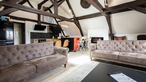 A loft-style living space with exposed wooden beams, a fireplace, and a modern kitchen.