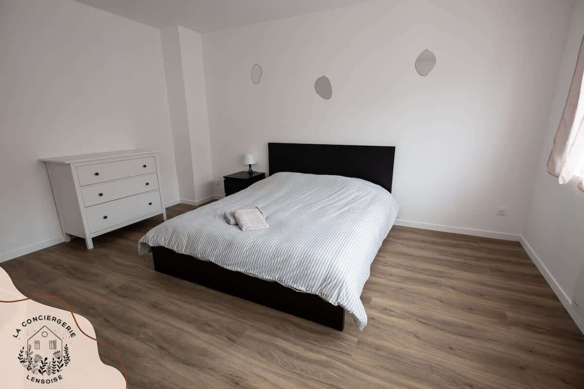 A bedroom with a bed, a dresser, a nightstand, and a wall-mounted light fixture.