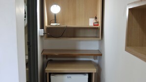 Una kitchenette compacta con refrigerador, una pequeña encimera y una estantería con una lámpara.