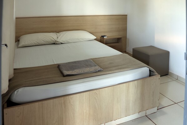 A modern bedroom with a wooden headboard, a bed with white linens, a bedside table with a lamp, and a small wooden nightstand.