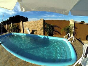 A swimming pool with clear water, surrounded by a stone wall and potted plants.