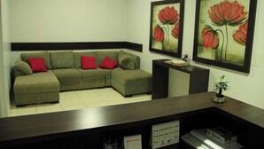Una sala de estar con un sofá modular, una mesa de centro y dos cuadros enmarcados con motivos florales en la pared.