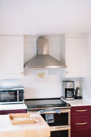 A kitchen with white cabinets, a stainless steel range hood, a microwave, a coffee maker, and a wooden cutting board. - 2BR Folly Cottage 1-block from the beach! (Folly Beach)