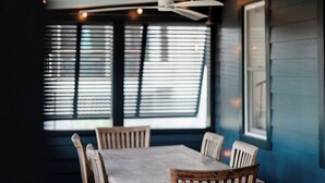 Un comedor con una mesa y sillas, un ventilador de techo y ventanas con persianas.
