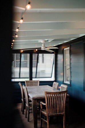 Ein Essbereich mit Tisch und Stühlen, einem Deckenventilator und Fenstern mit Jalousien.