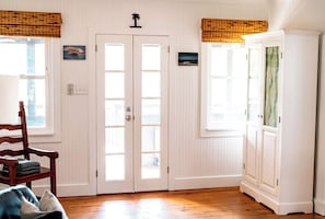 A room with a wooden floor, a white door with glass panels, a wooden chair, a cabinet with patterned curtains, and a small picture on the wall.