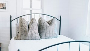 Una cama con estructura metálica y colchón blanco, acompañada de cuatro almohadas.