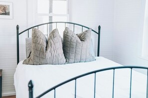 A bed with a metal frame and a white mattress, accompanied by four pillows. - 2BR Folly Cottage 1-block from the beach! (Folly Beach)