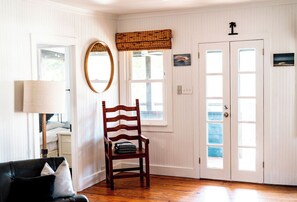 A room with a wooden chair, a lamp, a bed, and a door with windows.