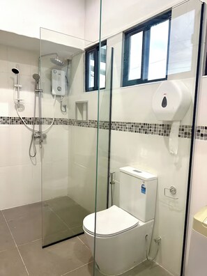 A modern bathroom with a glass-enclosed shower, a toilet, and a hand dryer.