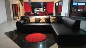 Una sala de estar moderna con un sofá de cuero negro, un tapete rojo y una cocina al fondo.