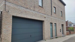 Un edificio de ladrillo de dos pisos con un gran portón para garage, un ventanal pequeño y una puerta con cerradura electrónica.