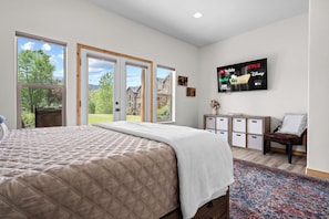 A bedroom with a large bed, a TV mounted on the wall, and a view through the door.