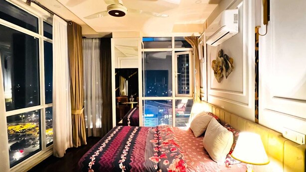Habitación de hotel con una cama grande, vista del paisaje urbano por la ventana y un ventilador de techo.