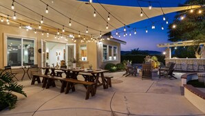 An outdoor patio with a wooden table and chairs, string lights, and a pergola. - Villa Verdot | 6BR Estate w/ Pool, Tennis, Basketball (Temecula)