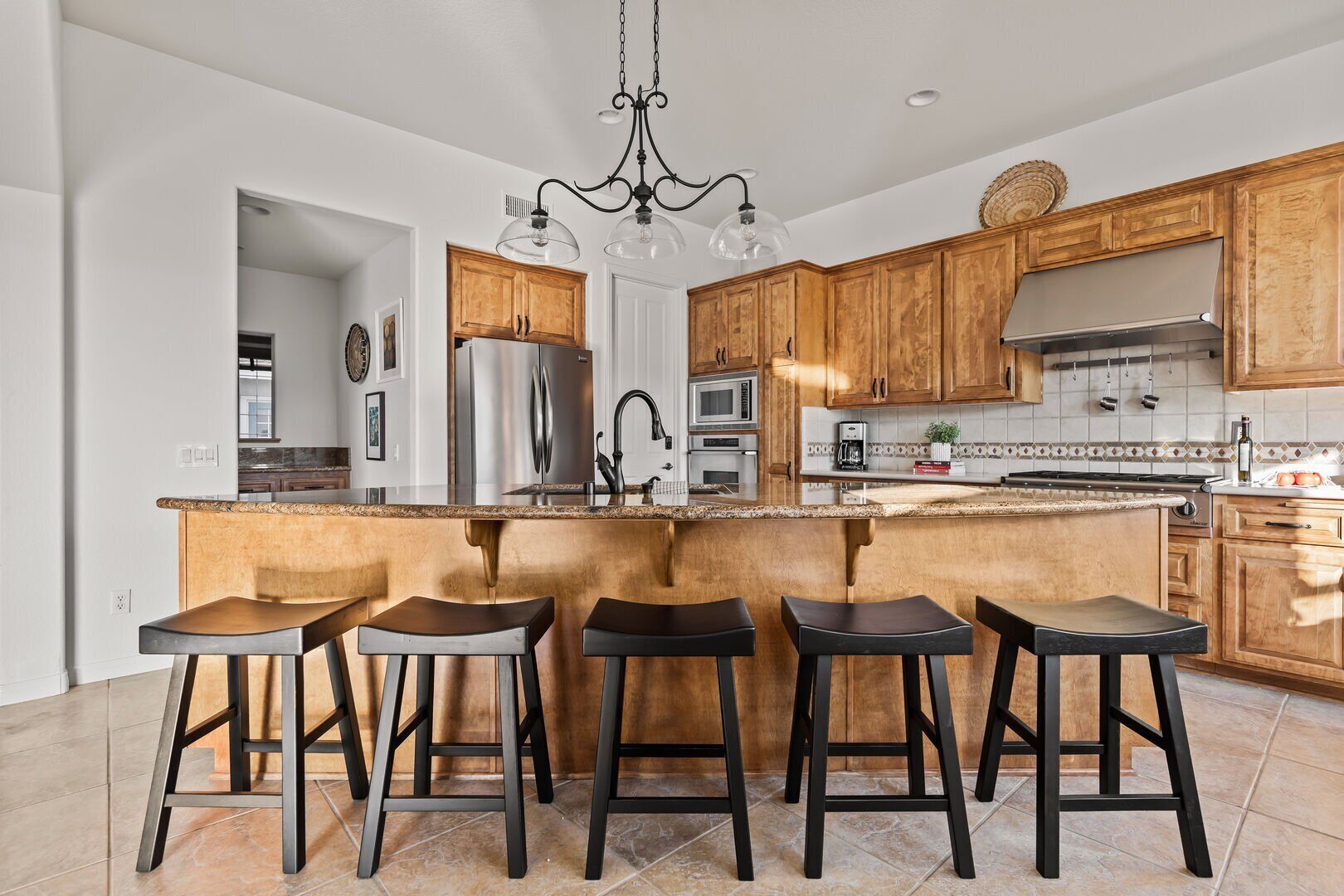 A modern kitchen with wooden cabinets, a stainless steel refrigerator, a gas stove, and a bar area with stools.