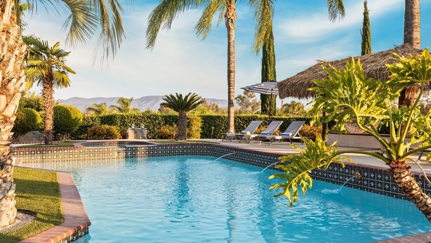A swimming pool with lounge chairs, palm trees, and a mountain view. - Villa Verdot | 6BR Estate w/ Pool, Tennis, Basketball (Temecula)