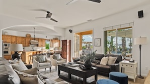 A spacious living room with a dark coffee table, leather sofas, and a view of the kitchen and outdoor patio. - Villa Verdot | 6BR Estate w/ Pool, Tennis, Basketball (Temecula)