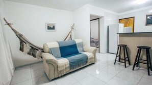 Un salon avec un canapé beige, une couverture bleue, un hamac et deux tabourets noirs.
