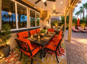 An outdoor dining area with a long table, orange cushioned chairs, and a ceiling fan. - Indio Casa Welcomes Everyone to stay and relax (Indio)