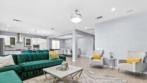 Amplia sala de estar con un sofá verde, un sillón blanco y una mesa de centro.