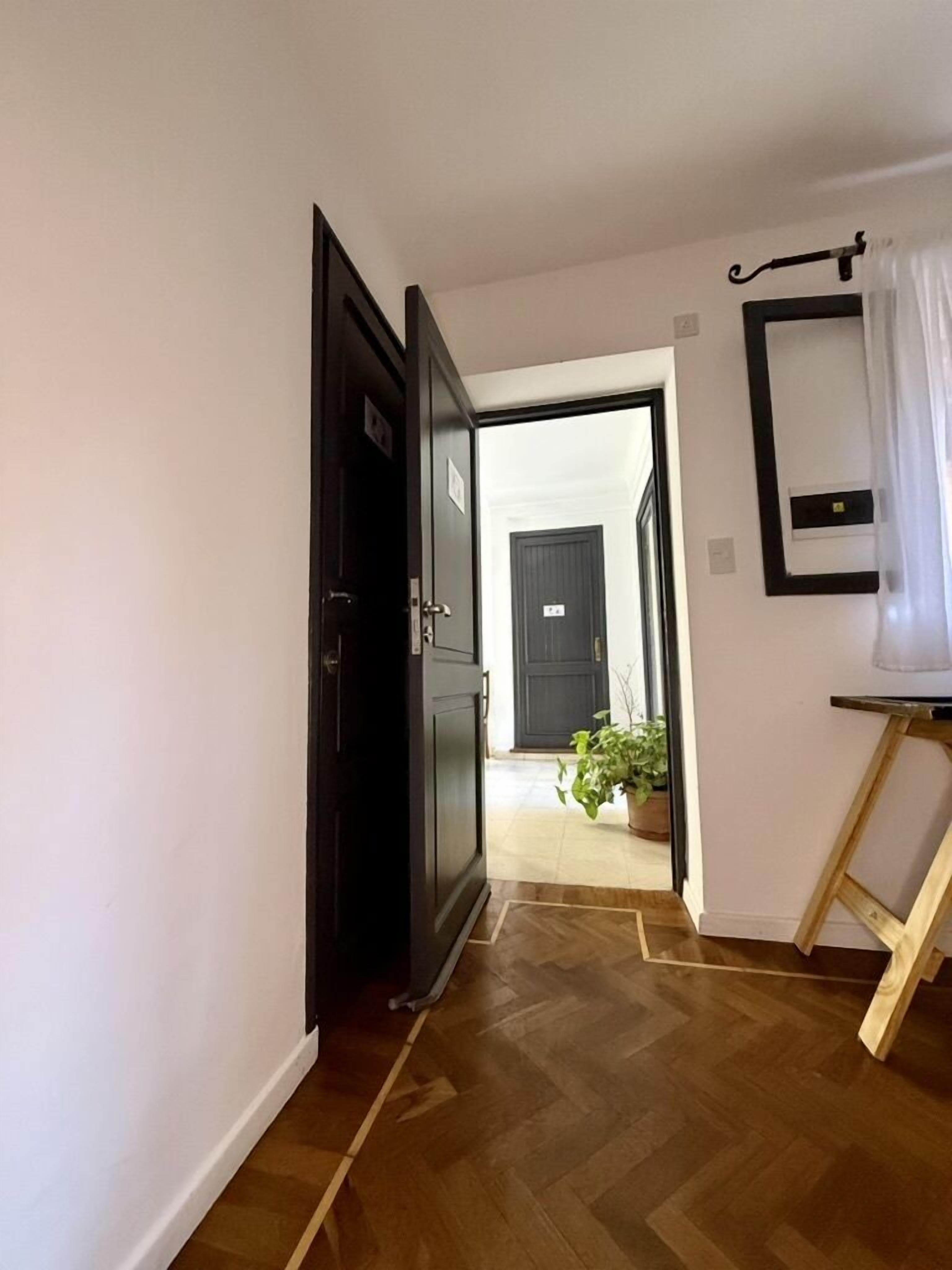 A hallway with a wooden floor, a dark door, and a small table with a mirror.