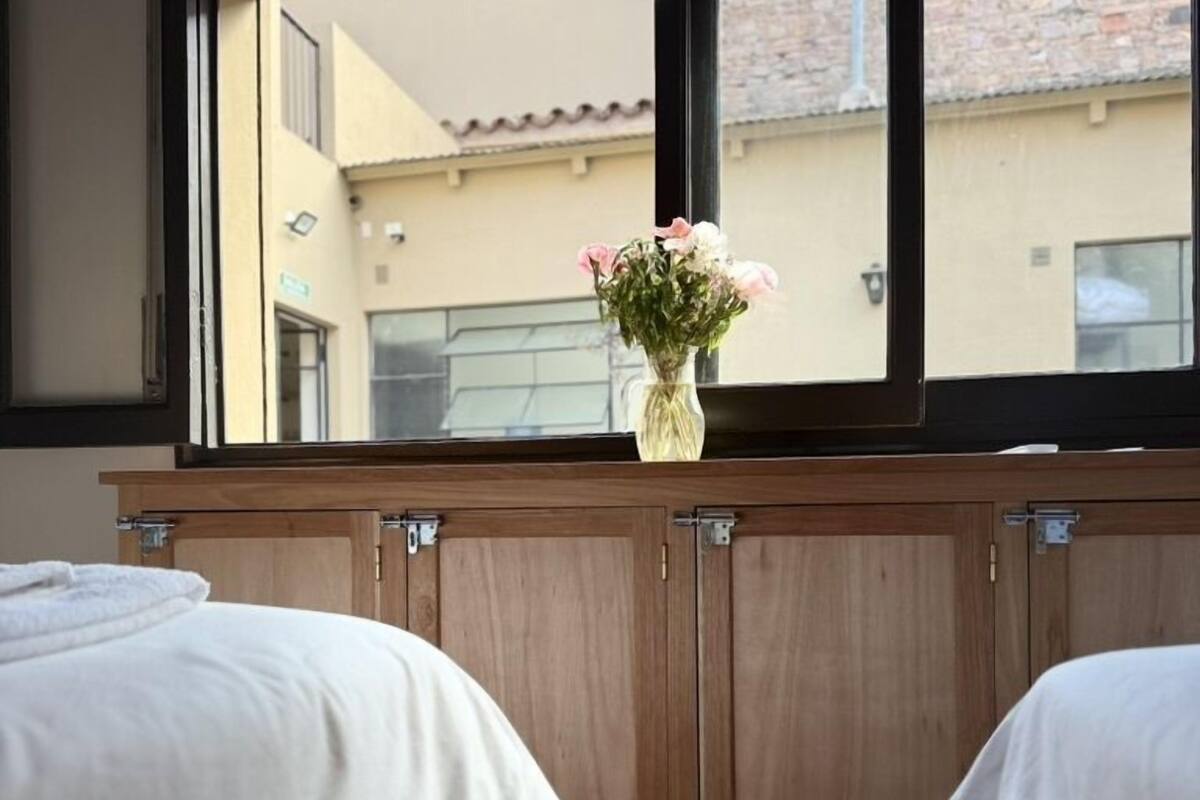 A bedroom with two beds, a wooden wardrobe, and a window with a view of buildings outside.