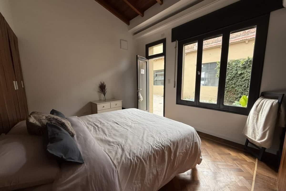 A bedroom with a bed, a nightstand, a dresser, and a window with a view of the outside.