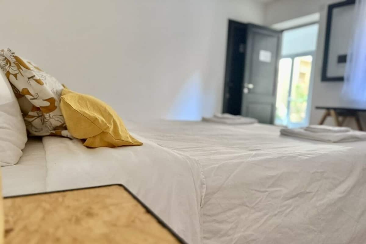 A hotel room with a bed, a wooden headboard, and a door leading to another room.