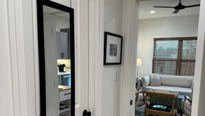 Un pasillo con una puerta blanca, un cuadro en la pared y vista a un salón con un sofá y una mesa de centro.