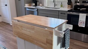 Una cocina con una isla central, armarios grises, un ventanal con cortinas y un horno de acero inoxidable.