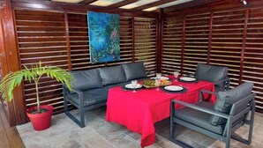 An outdoor dining area with a red tablecloth, two grey sofas, and a potted plant. - Le Havre de Paix (Le Moule)