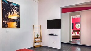 A modern bedroom with a bed, a TV, a painting, and a red wall. - Le Havre de Paix (Le Moule)