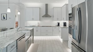 Une cuisine moderne avec des meubles blancs, des appareils en acier inoxydable et un plan de travail en marbre.